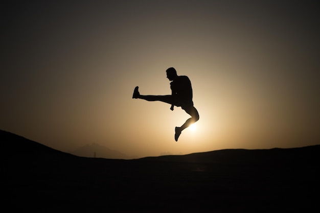 Silhouette of sportsman. Freedom, energy concept. Man jump on sunset sky background. Sport, fitness, activity. Athlete with muscular body in dusk.