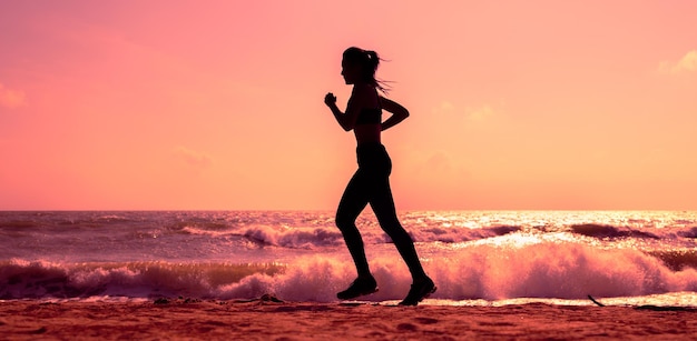 日没や日の出のビーチで走っているスポーティな女性のシルエット