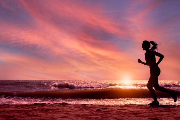 Силуэт спортивной девушки, бегущей на пляже на закате или восходе солнца