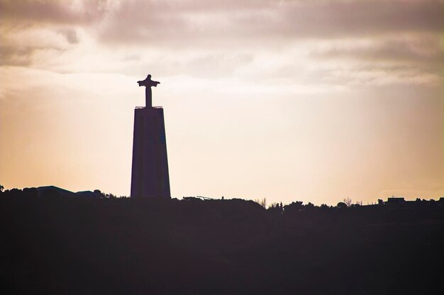 Silhouette of a statue of Christ in the background of the setting sun in Lisbon, Portugal.