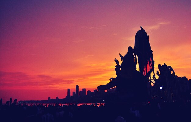 Photo silhouette of statue in city during sunset