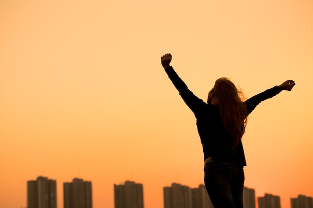 Silhouette success woman hands up with sunset sky background