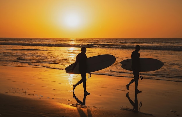 夕日の海のビーチでサーフボードを運ぶサーファーの人々のシルエット