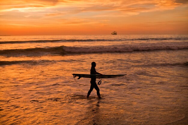 Silhouette of a surfer with a surfboard on the background of a golden sunset in the pacific ocean