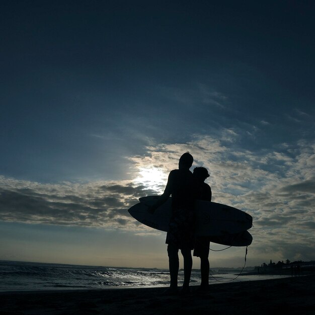 Foto surfista a silhouette con le tavole da surf in piedi sulla spiaggia contro il cielo