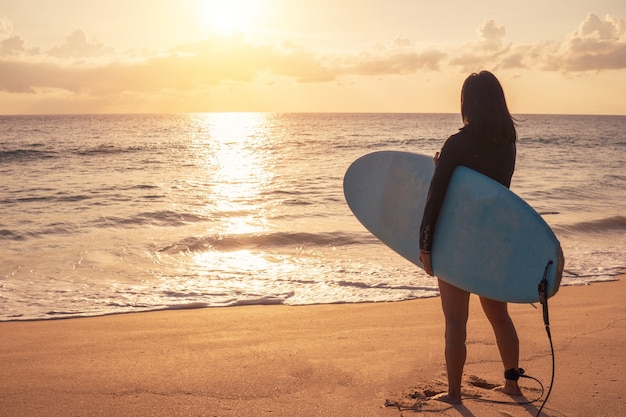 Silhouette of surfer woman carrying their surfboards on sunset beach with sun light 