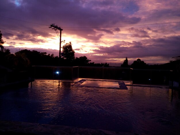 Silhouette swimming pool by lake against sky during sunset