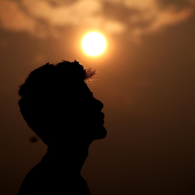 Silhouette teenage boy against orange sky