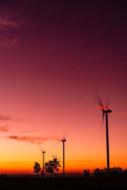 Силуэт трех современных ветряных мельниц на красноватом закате на окраине Кию Сан-Хосе Уругвай