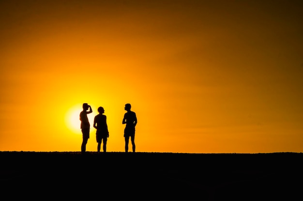 Photo silhouette of three persons in an orange background