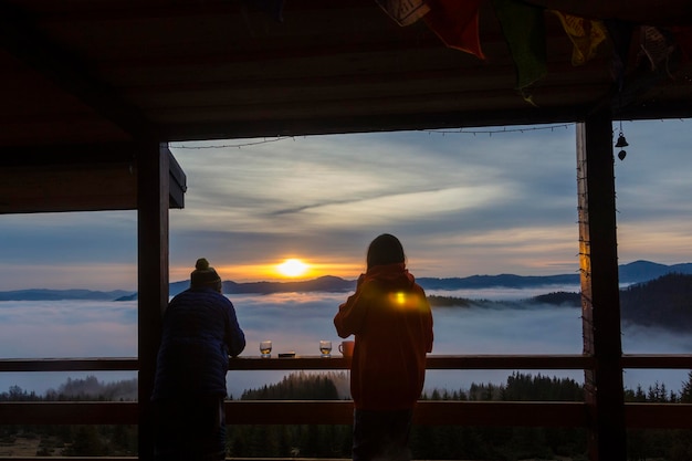 雲に覆われた霧の山々でオレンジ色の朝日を楽しむ観光客のシルエット