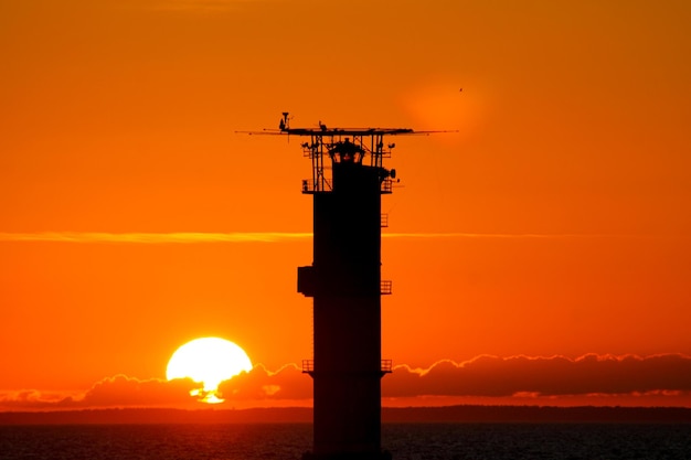 Silhouette of tower by sea against orange sky