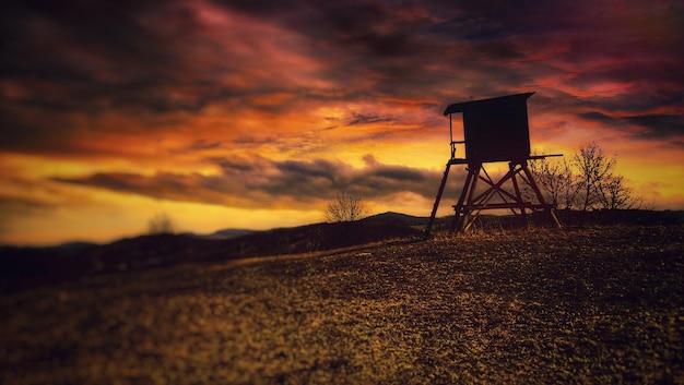 Silhouette tower on field against sky during sunset