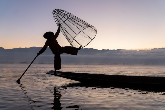 silhouette of traditional fisherman with boat on inle lake during sunrise against sky