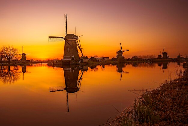 Silhouette of traditional windmill by lake against sky during sunset