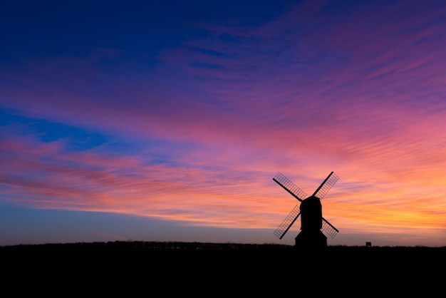 Silhouette traditional windmill on field against sky during sunset