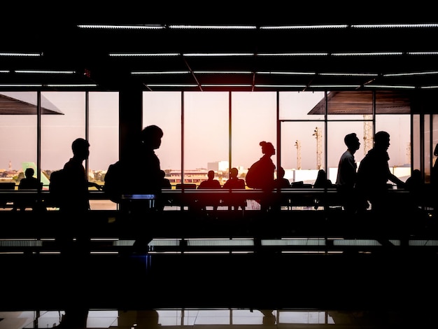 Silhouette travelers walking on moving walkway in airport terminal