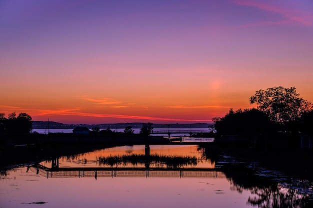 Silhouette trees by lake against romantic sky at sunset