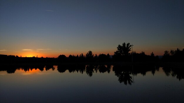 Silhouette trees by lake against sky during sunset