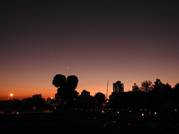 Photo silhouette trees and illuminated city against sky at sunset