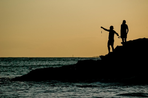 silhouette of two fishermen on a beach at sunset