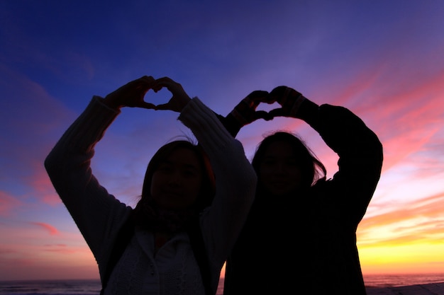 Photo silhouette of two grils forming thier hand to heart shape