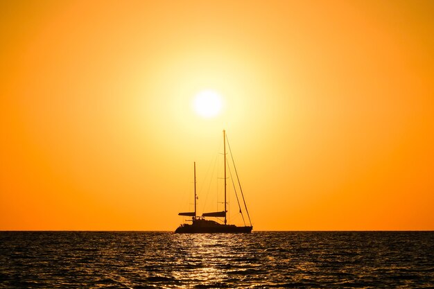 Foto silhouette di uno yacht a due alberi in mare sullo sfondo dell'orizzonte del sole al tramonto.