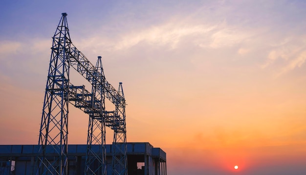 Silhouette unconnected high voltage electric pylons and power station building at sunset