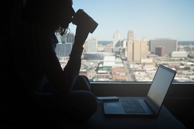 Silhouette di una donna irriconoscibile che beve caffè mentre lavora al computer, concetto di nomade digitale, spazio di copia