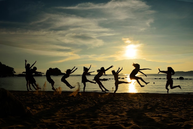 Silhouette vrienden springen op het strand tegen bewolkte lucht tijdens zonsondergang