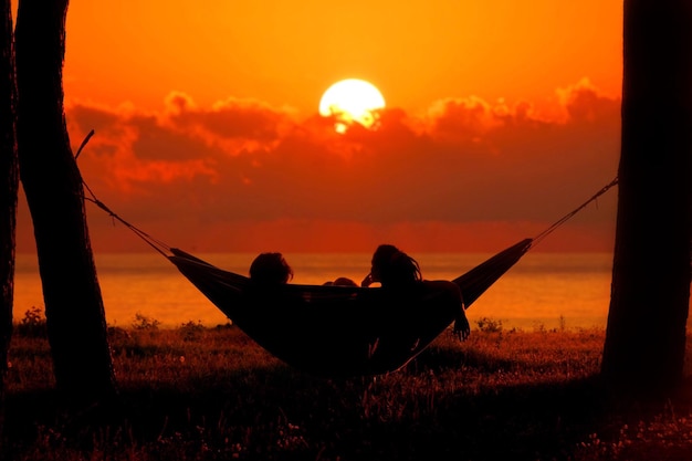 Foto silhouette vrienden zitten in een hangmat tegen de hemel tijdens de zonsondergang