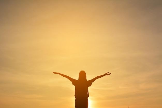 Silhouette vrouw met uitgestrekte armen tegen de hemel tijdens zonsondergang