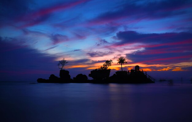 写真 ボラカイの日没時雲の空に照らされた海の中のシルエット・ウィリー・ロック