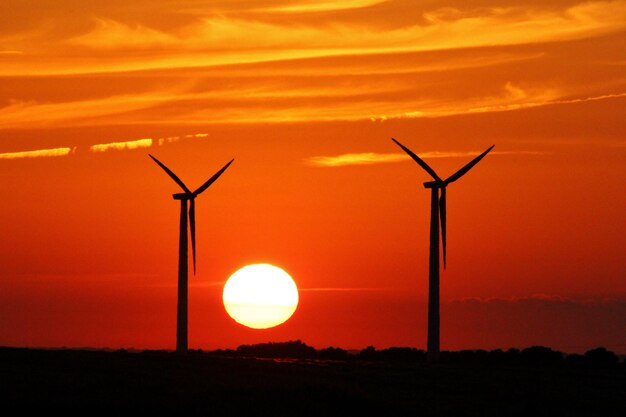 Silhouette wind turbine against orange sky