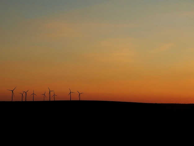 silhouette wind turbines on field against orange sky during sunset