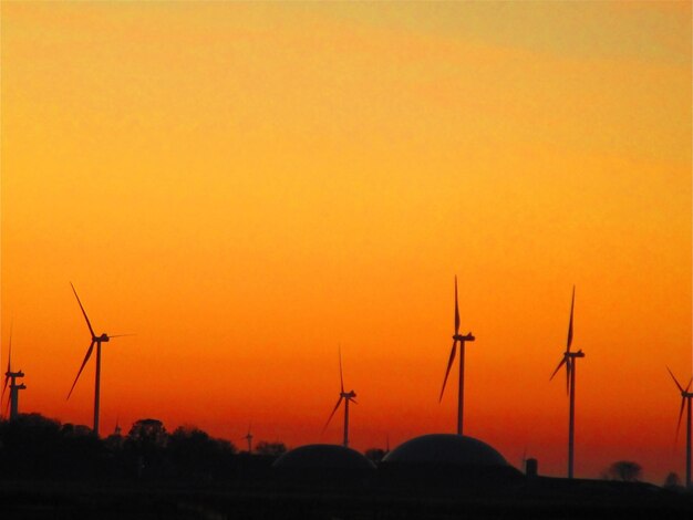 Silhouette wind turbines on field against orange sky