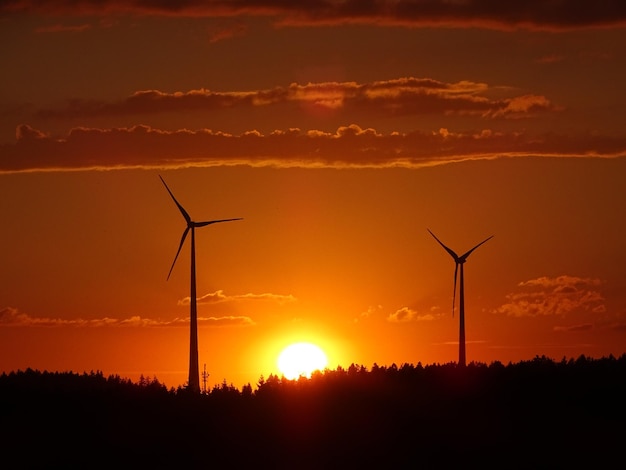 Silhouette wind turbines on field against sky during sunset