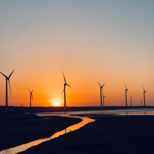 silhouette wind turbines on land against sky during sunset