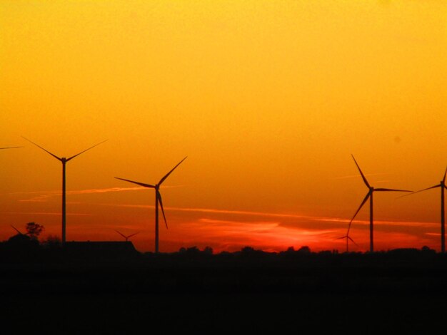 Silhouette wind turbines on landscape against sky during sunset