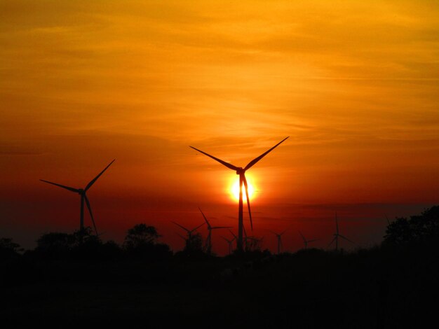 Silhouette wind turbines on landscape against sky during sunset