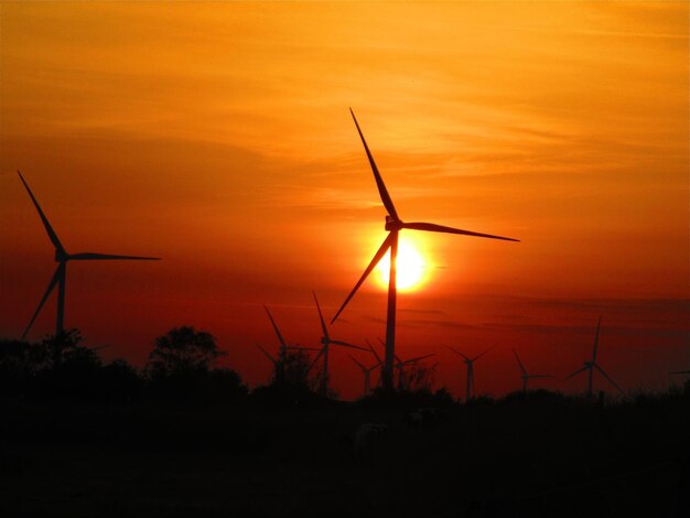 Silhouette windmill on field against romantic sky at sunset