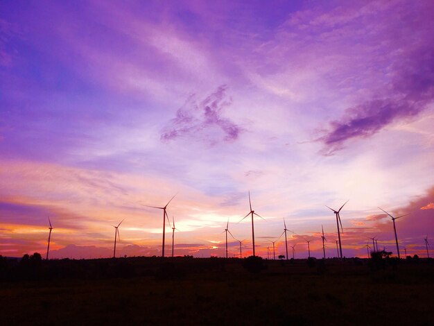 Silhouette windmills on field against sky during sunset