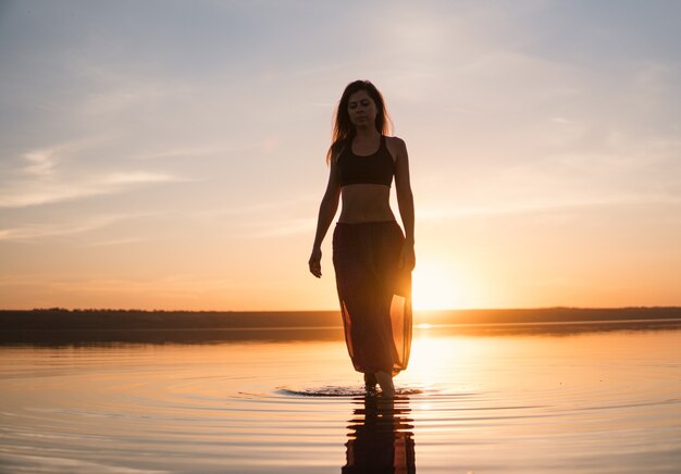 Silhouette woman on the beach at sunset doing yoga asana. Morning natural stretch warm-up training