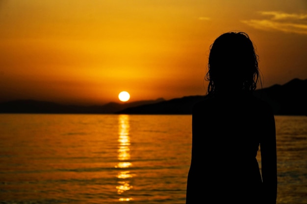 Foto silhouette di una donna sul mare contro il cielo durante il tramonto