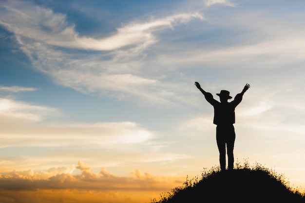 silhouette of woman celebrating success on top of a hill in the sunset