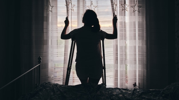 Silhouette of a woman on crutches by the window. rehabilitation\
after physical trauma.