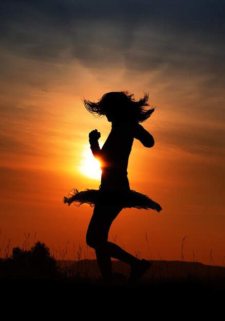Foto donna a silhouette che balla sul campo contro il cielo arancione