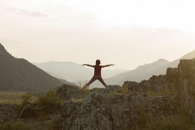 silhouette of woman doing yoga or qigong in mountains at sunset in summer