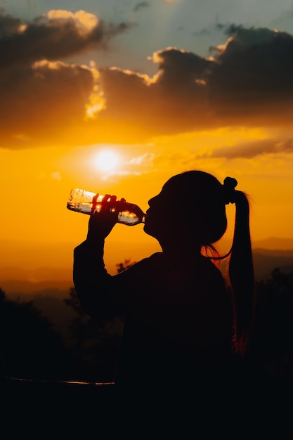 Siluetta di una donna che beve acqua potabile al tramonto
