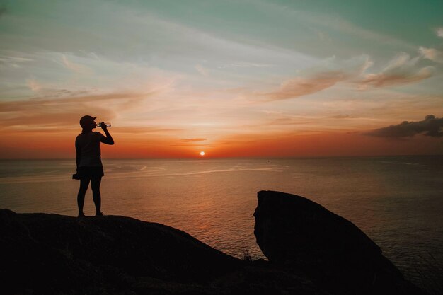 Photo silhouette woman drinking water at sea against sky during sunset